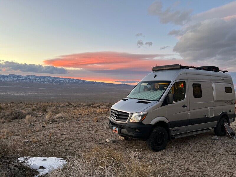 An RV rental, a grey Mercedes-Benz camper van, parked in a vast desert landscape with mountains under a vibrant sunset. — photo 3