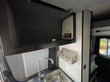 View of a modern RV rental kitchenette with a stainless steel sink, sleek chrome faucet, overhead cabinet, and wall-mounted shelf.