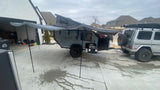 This **RV rental** setup features an overland trailer with an extended awning and outdoor kitchen, hitched to a G-Wagon in a driveway.