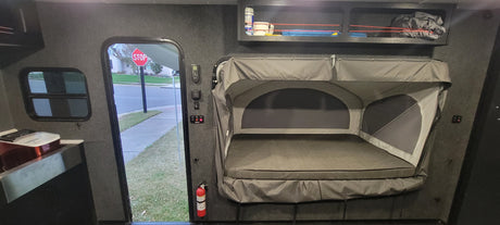 Inside an rv rental: a pop-up bed, controls, window & open door looking at a stop sign on a residential street.