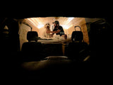 Cozy RV rental interior shows a man and his fluffy dog on a bed with wood paneling, viewed from the driver's seat.