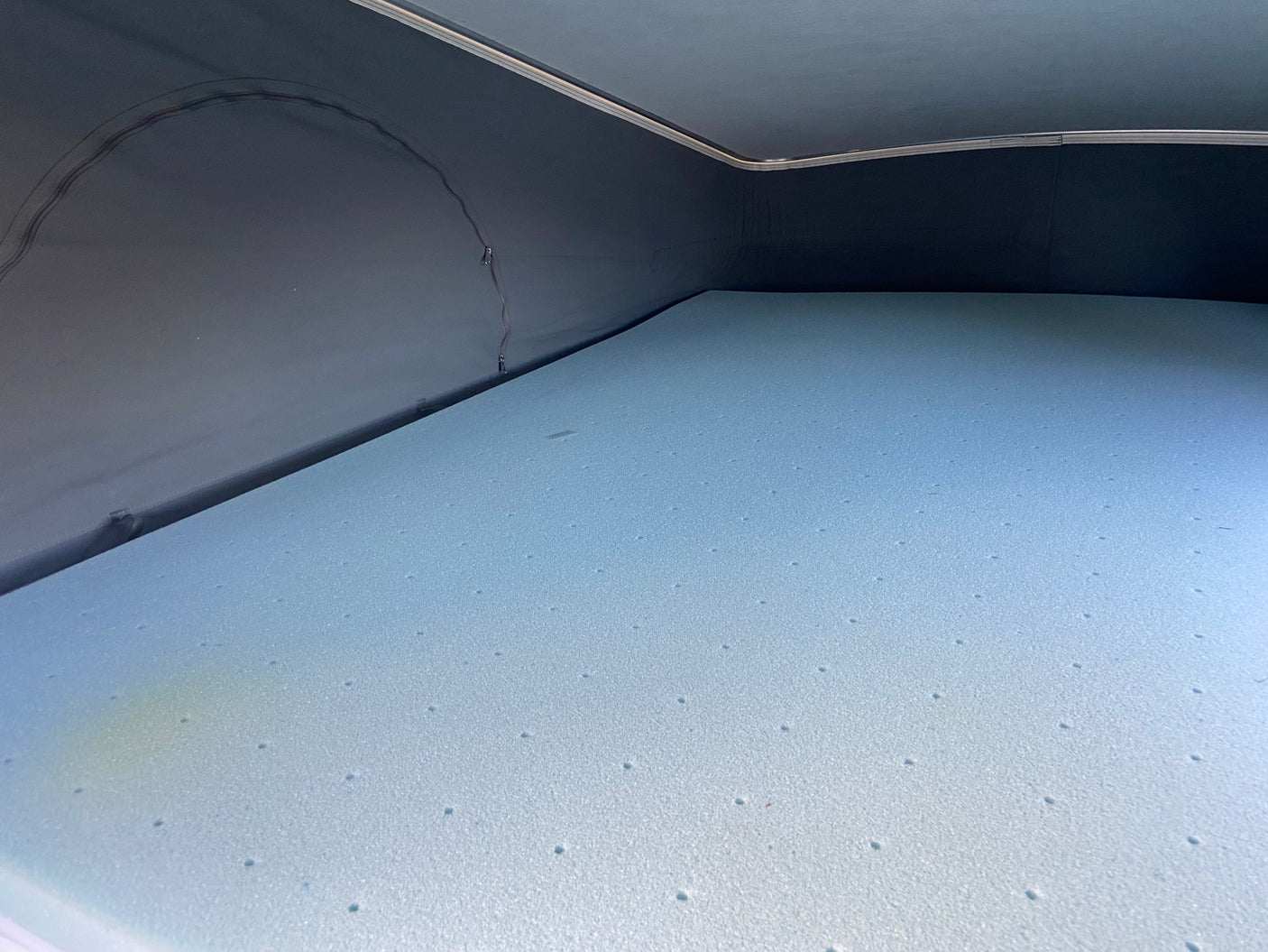 RV rental camper interior: light blue foam mattress in the sleeping area with dark fabric walls showing some streaks.