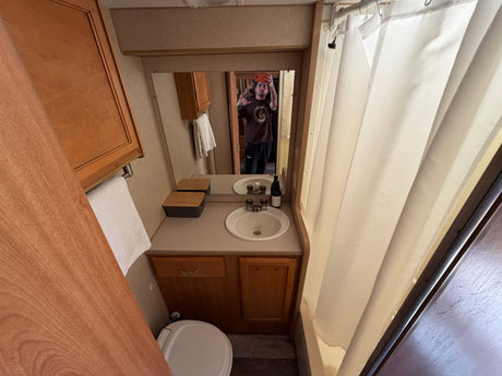 Compact RV rental bathroom featuring a sink, mirror, toilet, and shower with a curtain.
