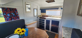 Cozy RV rental interior featuring a compact kitchen, dining area, and fun map curtains. Perfect for your next road trip adventure.
