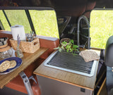 This RV rental features a compact kitchen with a sink, faucet, breakfast bagels, coffee maker, and a green outdoor view.