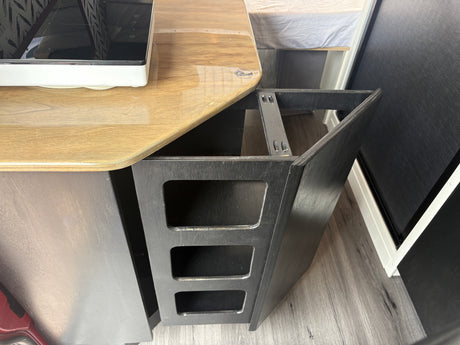 RV rental interior featuring a compact kitchenette on a wooden counter, a black open storage unit, and an adjacent bed.