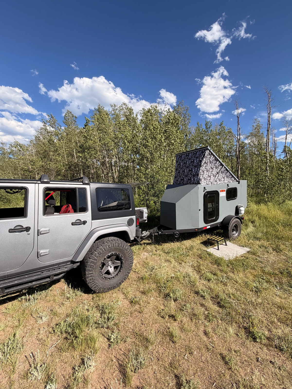 A gray Jeep towing a pop-top camper (for sale) with camo roof, parked in grassy area against trees. Great for RV rental adventures. — photo 10