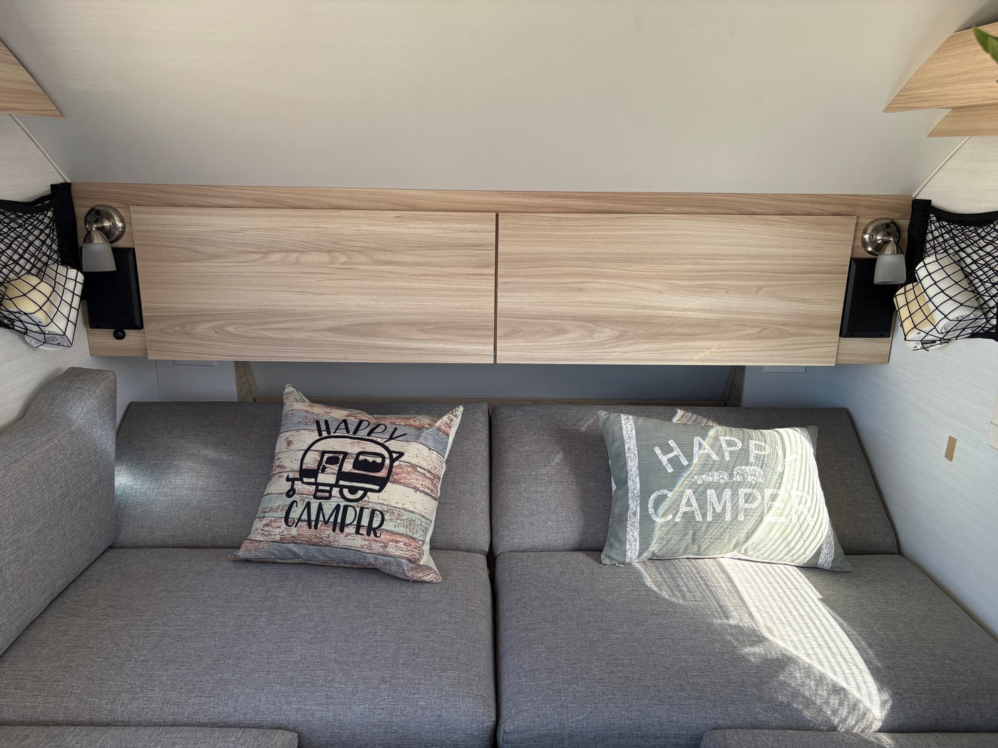 Cozy rv rental interior with grey seating, "Happy Camper" pillows, overhead storage, and reading lights. — photo 5