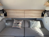 Cozy rv rental interior with grey seating, "Happy Camper" pillows, overhead storage, and reading lights.