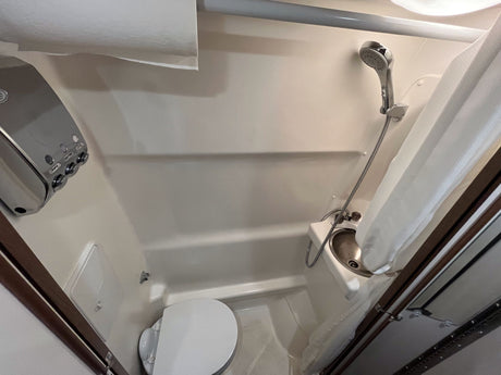 This RV rental compact bathroom features a white interior with a toilet, shower, and small sink for efficient space utilization.