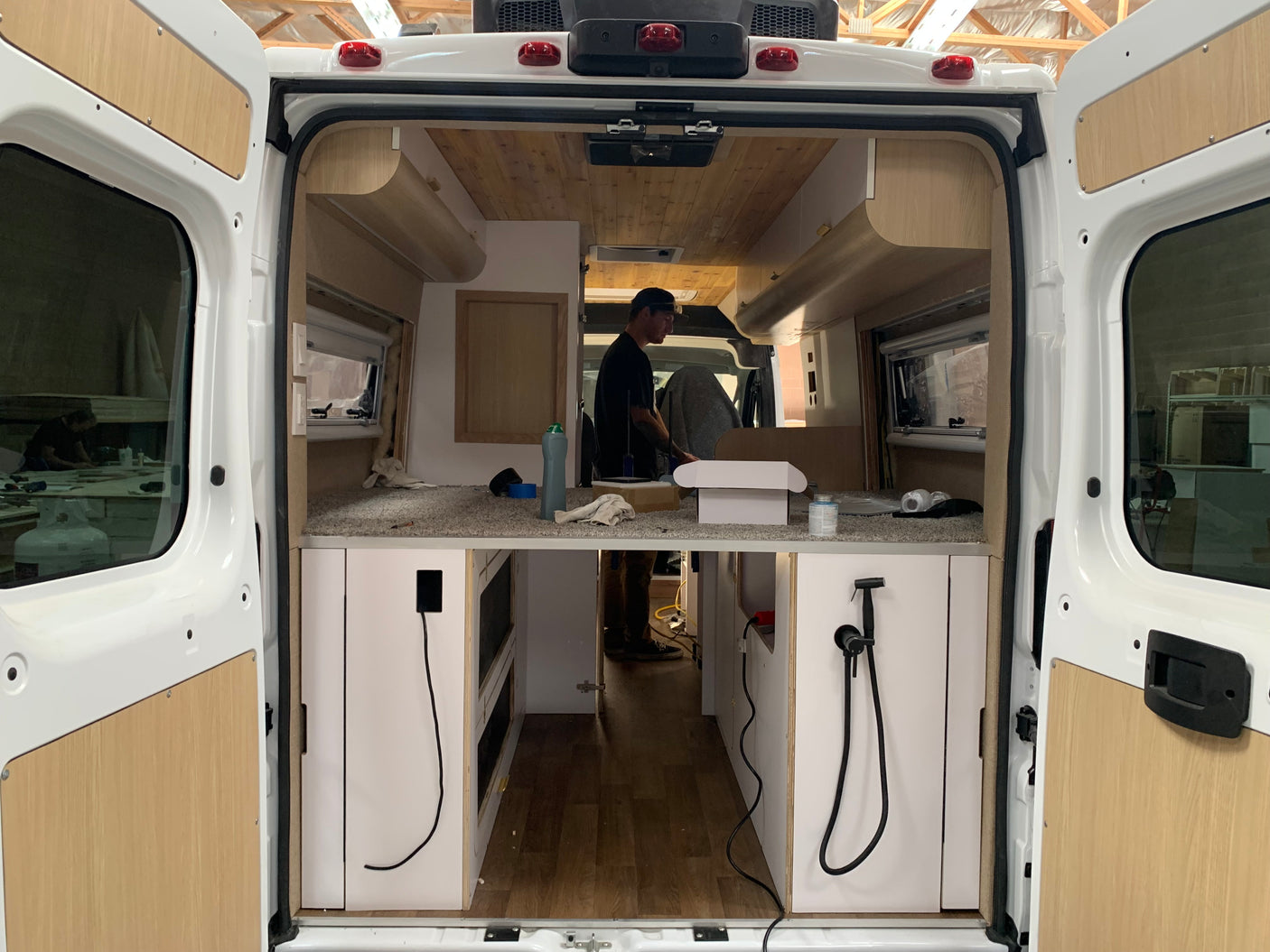 Inside an RV rental van during its conversion: view of custom cabinetry, wood paneling, and an ongoing build.