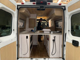 Inside an RV rental van during its conversion: view of custom cabinetry, wood paneling, and an ongoing build.