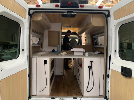 Inside an RV rental van during its conversion: view of custom cabinetry, wood paneling, and an ongoing build.