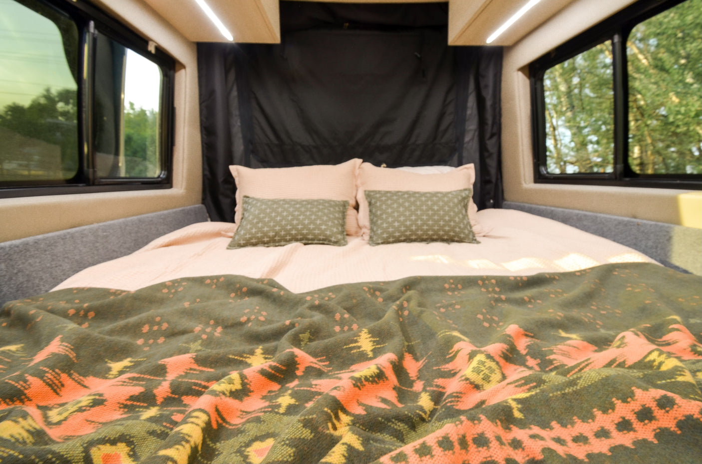 Comfortable RV rental bedroom featuring a full bed with cozy pink sheets, patterned pillows, and scenic window views.