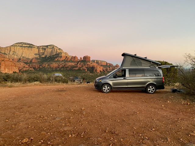 Grey pop-top camper van RV rental on red dirt, perfect for Sedona red rock camping. Scenic outdoor adventure.