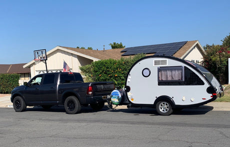 This RV rental setup, a dark grey truck pulling a teardrop camper, sits on a sunny residential street. Ready for travel!