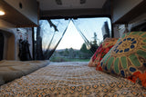Cozy rv rental bed with patterned sheets and pillows, offering a scenic outdoor view through the open rear doors.