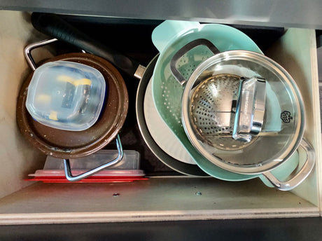 Organized kitchen drawer in an RV rental: pan, colander, pot, plates, & containers. Space-saving storage for camping.