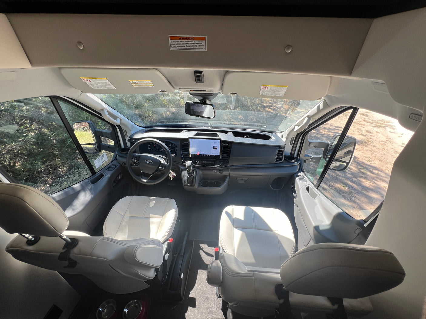RV rental interior: Cockpit view with modern dashboard, large screen, steering wheel, and comfortable swivel front seats.