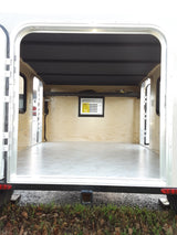 Compact RV rental interior featuring wooden walls, a built-in sleeping area, and a window AC unit. Ideal for travel.