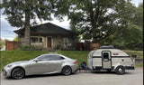 A Lexus sedan tows a compact Little Guy teardrop RV rental on a residential street. Ready for a cozy road trip adventure.