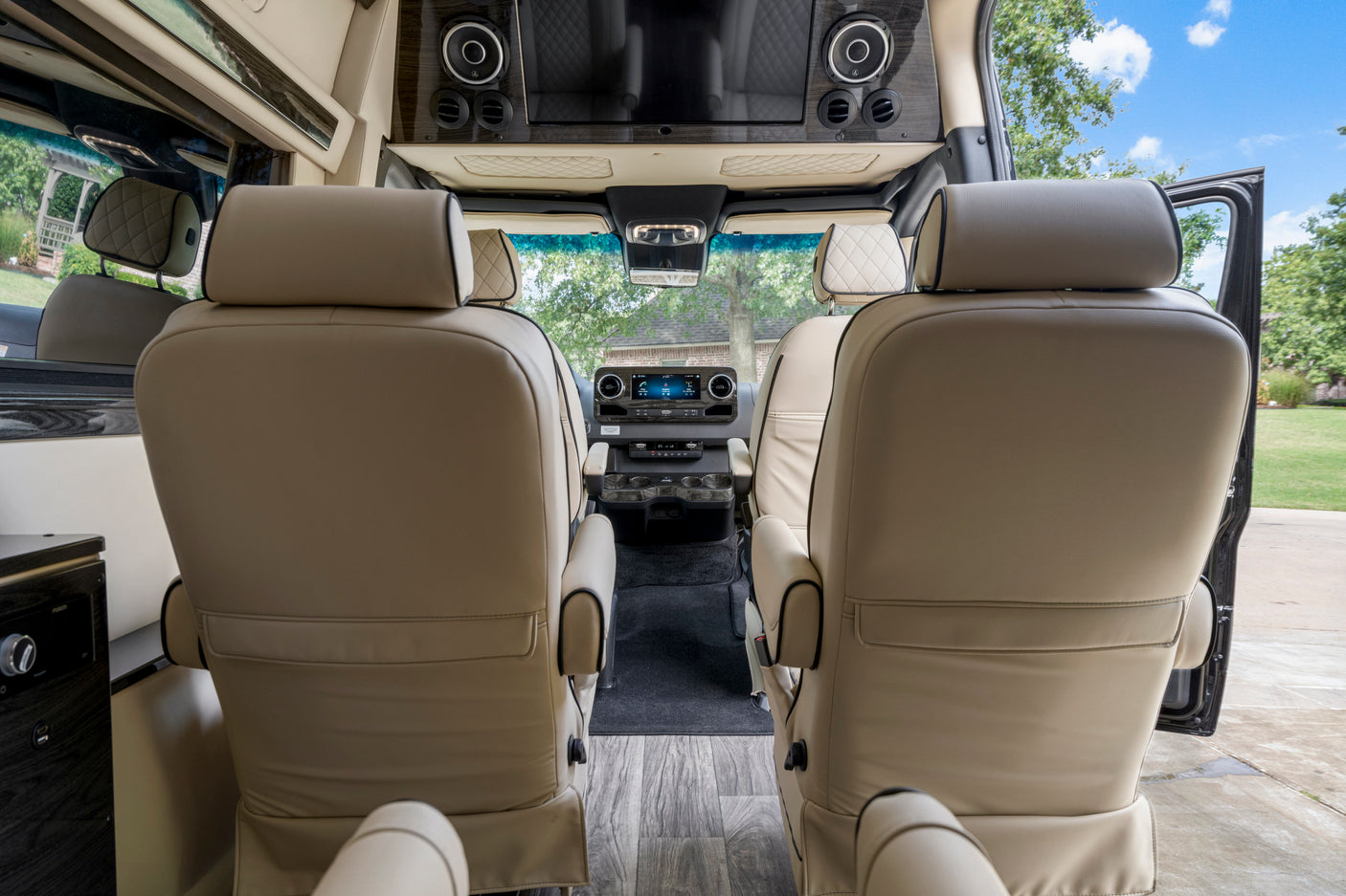 Spacious RV rental interior. View from rear shows two plush passenger seats, the driver's cockpit, & entertainment system.
