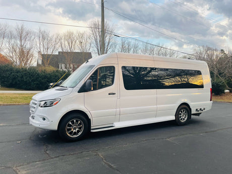 Spacious white Mercedes Sprinter RV rental van parked on asphalt. Reflections of trees & sunset in windows. Adventure awaits!