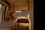 Cozy RV rental interior: A modern camper van with a bed, kitchen, and a desert view through the back window.