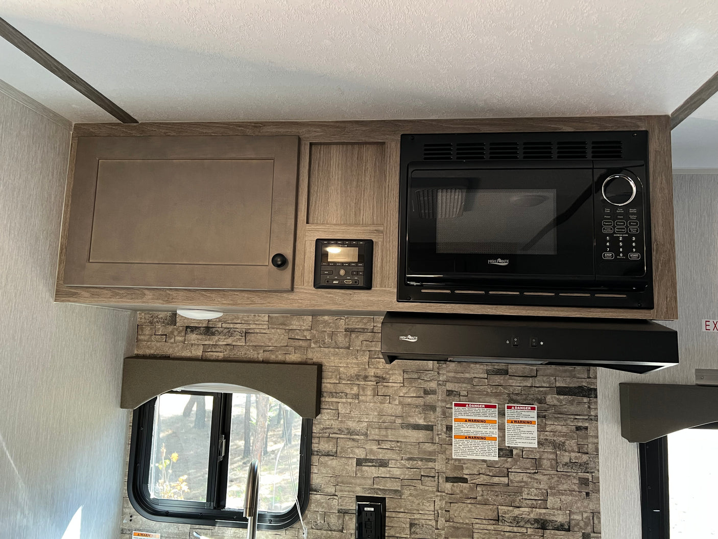RV rental kitchen with wood-look cabinets, High Pointe microwave & range hood, control panel, and stone backsplash.