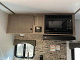 RV rental kitchen with wood-look cabinets, High Pointe microwave & range hood, control panel, and stone backsplash.