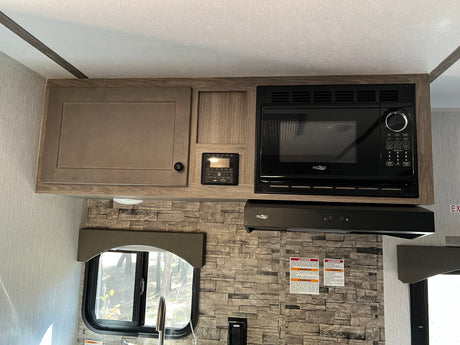 RV rental kitchen with wood-look cabinets, High Pointe microwave & range hood, control panel, and stone backsplash.