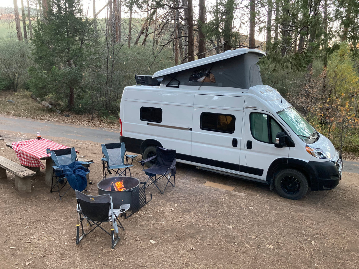 Relaxing at a wooded campsite with a pop-top RV rental, featuring a warm campfire, picnic table, and chairs.