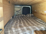 This **RV rental** features a cozy sleeping area with plaid bedding, wood-paneled walls, and roadrunner artwork.