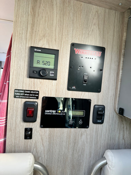 Inside an RV rental, showing various control panels: Truma heater, Winnebago water pump, tank levels, and Xantrex solar charge controller.
