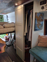 RV rental interior with an elevated bed, open closet, and nature view from rear doors, showcasing compact living.