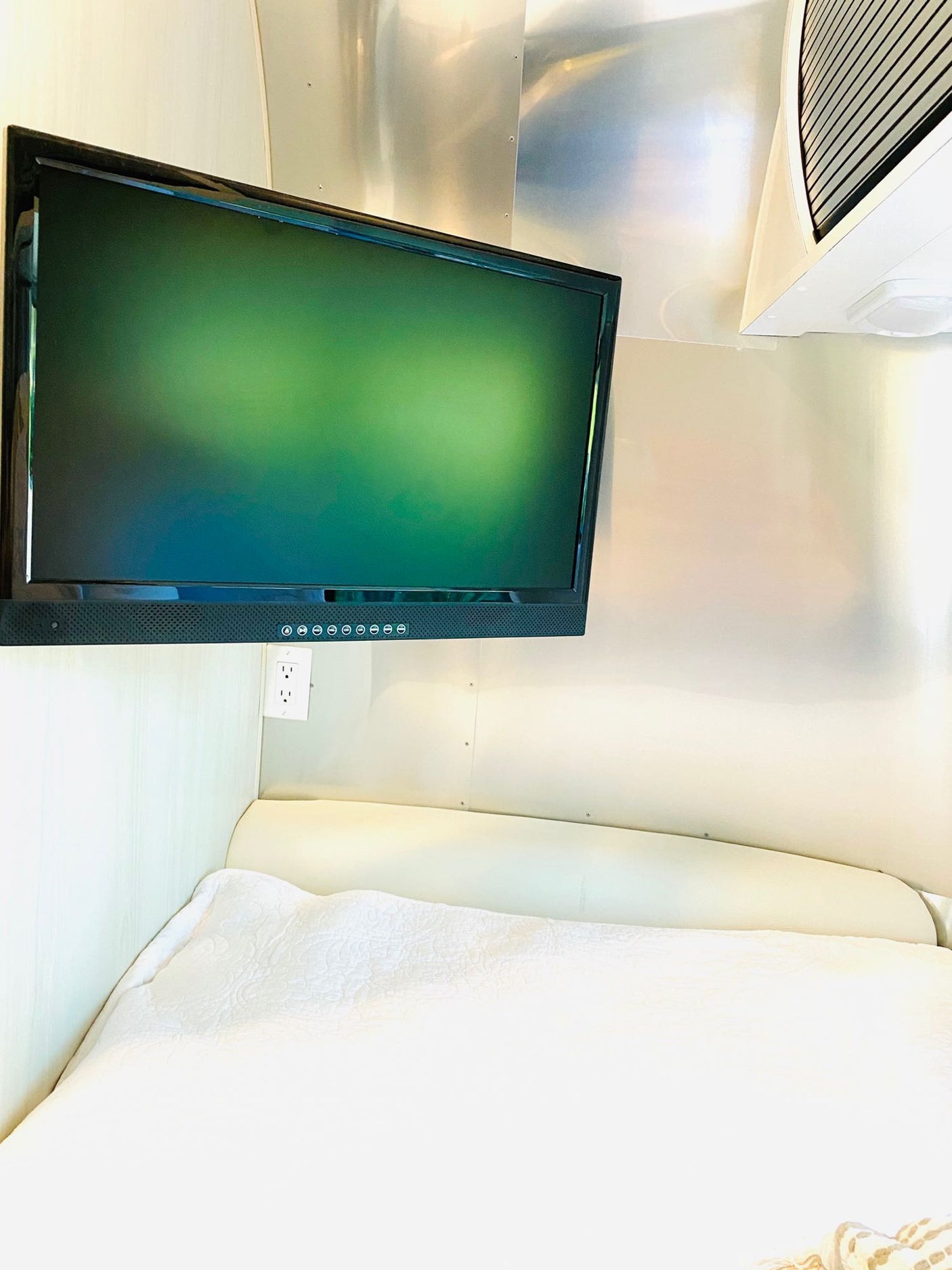 Enjoy this RV rental's cozy interior, featuring a comfortable bed, mounted TV, and convenient power outlet.