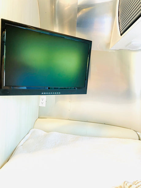 Enjoy this RV rental's cozy interior, featuring a comfortable bed, mounted TV, and convenient power outlet.