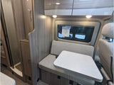 Step inside this RV rental showcasing a compact dinette with table, overhead cabinets, and a small shower area.