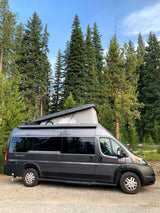 Gray pop-top camper van for rv rental, parked among tall trees. Perfect for camping in nature.