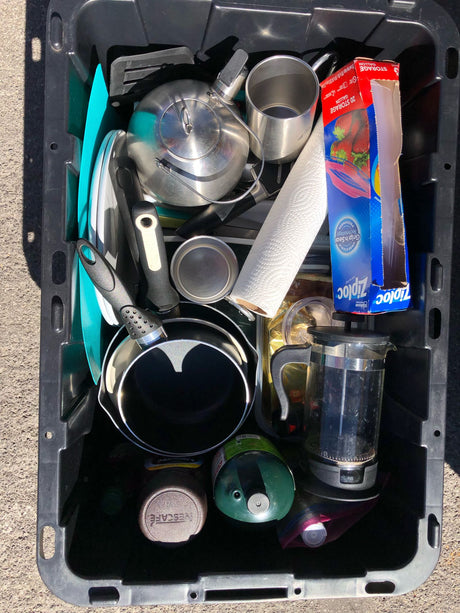 Get ready for your RV rental adventure! Packed bin of camping kitchen essentials: pots, kettle, French press, propane.