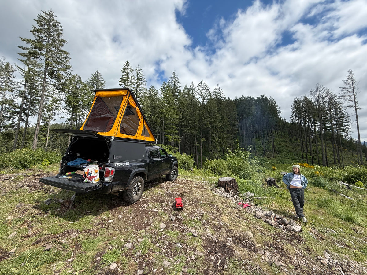 A black pickup truck with an orange rooftop tent, and a person in a forest clearing. Great rv rental option for wilderness camping. — photo 2