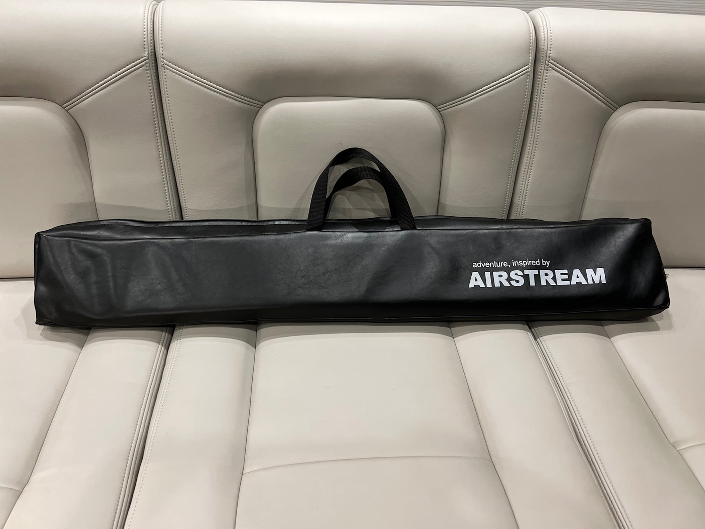 An Airstream branded accessory bag rests on a cream leather RV rental seat, ready for adventure.