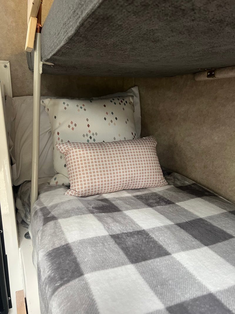 Cozy RV rental bunk bed features a gray buffalo check blanket, white and pink patterned pillows, offering a comfortable interior. — photo 10