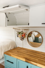 RV rental interior: Bright and organized, featuring a hanging fruit basket, butcher block counter, and cozy bed.