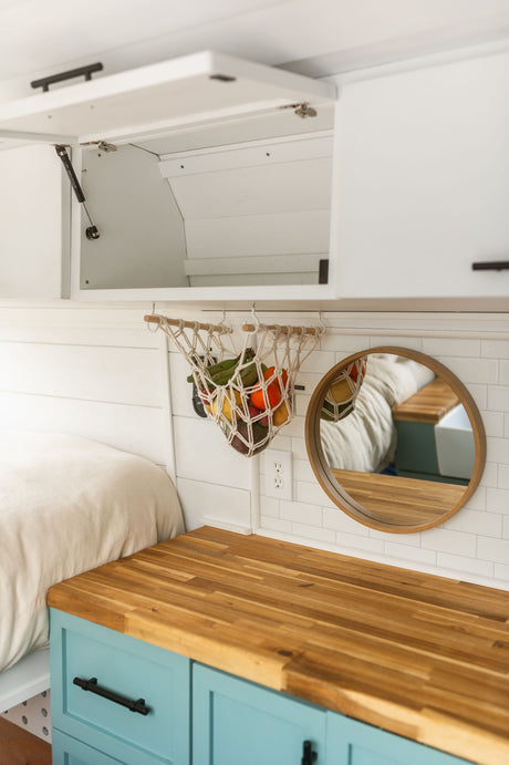 RV rental interior: Bright and organized, featuring a hanging fruit basket, butcher block counter, and cozy bed.