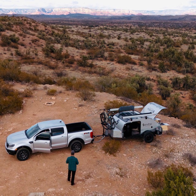 A silver pickup tows a teardrop camper with bikes attached