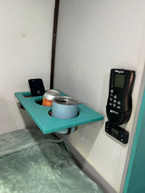 Cozy RV rental bedroom with a teal bedside shelf holding a phone, canned drink, and mug, alongside climate controls.