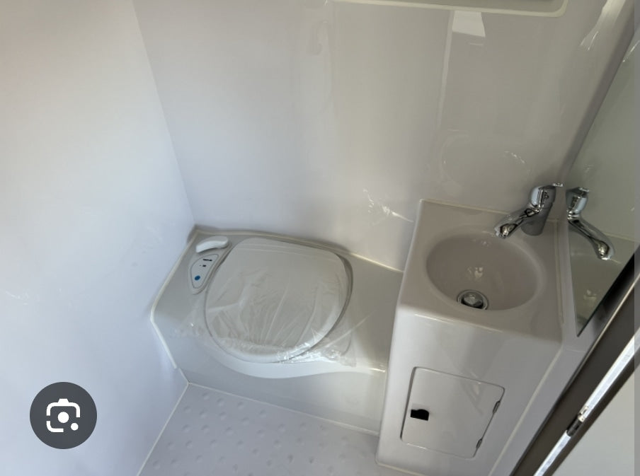 Compact RV rental bathroom with plastic-covered toilet, sink, and mirror.