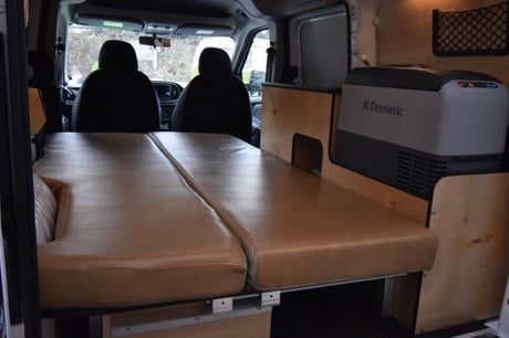 Inside an RV rental camper van: comfortable tan bed cushions, custom wood interior, and a Dometic fridge. Ready for adventure!