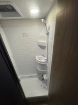 Compact white shower in an RV rental, featuring a handheld showerhead and small corner sink. Ideal for travel.